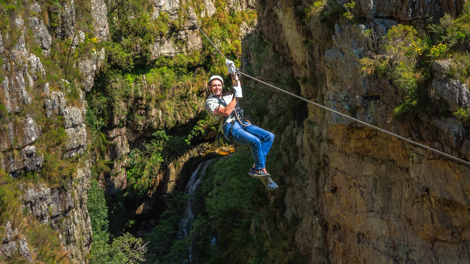 A guest smiling mid-slide on a zipline high above a gorge in the Hottentots Holland Nature Reserve near Cape Town